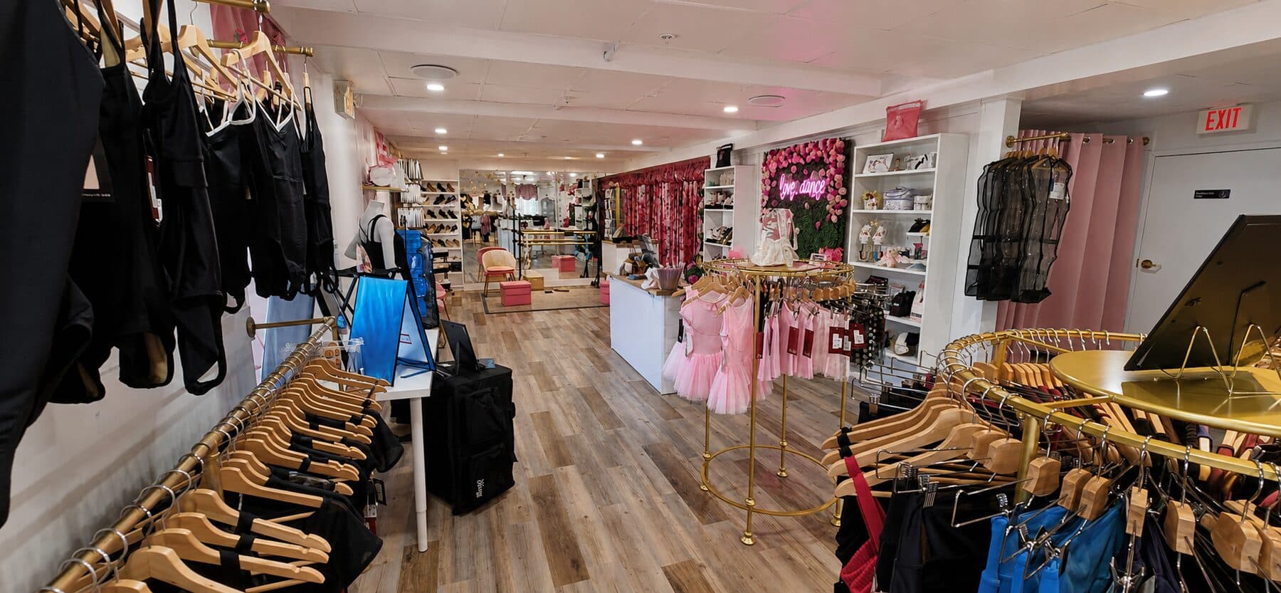 Boutique interior with a wall of leotards, a shoe display, and pink fitting-room curtains.